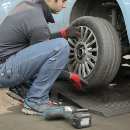 Mechanic changing a car tire indoors, using tools for vehicle maintenance.
